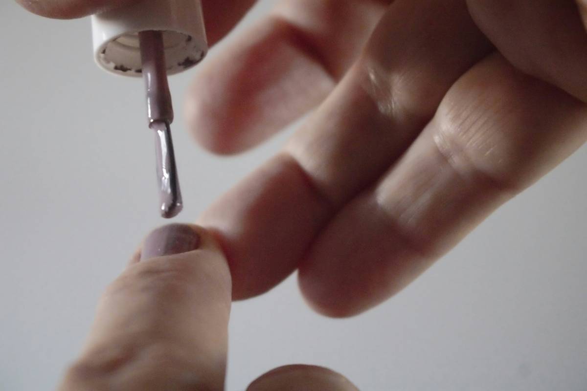 how to clean nail clippers: close-up photo of stainless steel nail clippers submerged in small glass bowl of isopropyl alcohol, with cotton swab and soft brush beside it